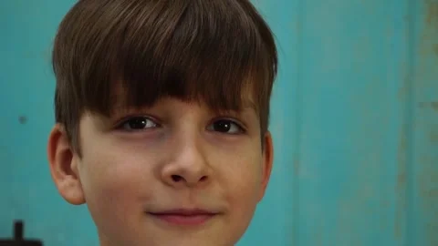 A nine-year-old boy stands and looks at the blue wall at the camera. Slow motion Stock Footage 245911582