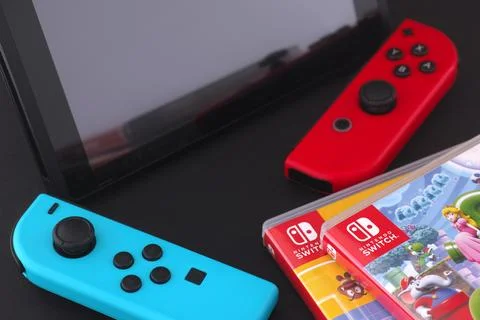A Nintendo Switch console with detached joy-cons lying near a stack of games Stock Photos