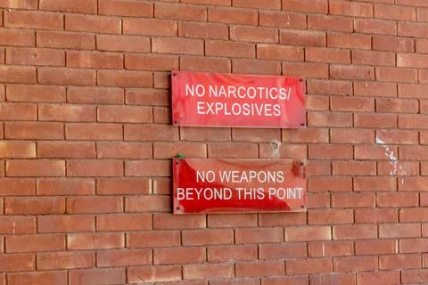 No narcotics explosives no weapons beyond this point signs on a brick wall Stock Photos