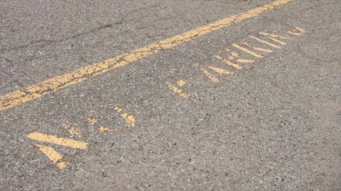 No parking caption print text writing in yellow below line on pavement, worn Stock Footage 247749091