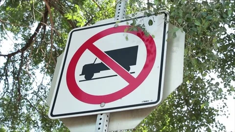 No trucks allowed square sign on metal post with stop sign behind and tree Stock Footage 252043316
