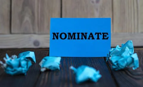 NOMINATE - words on blue paper on a dark wooden background with crumpled piec Stock Photos