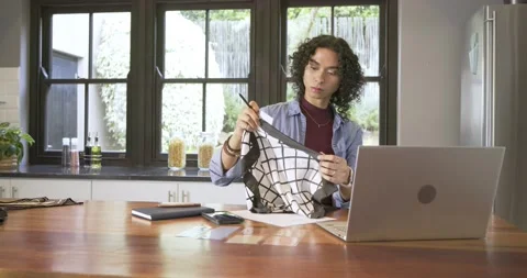 Non-binary adult picking up grid cloth in kitchen, unfolding design, noting, Stock Footage 341393194