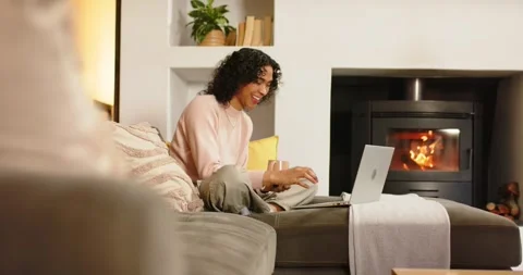 Non-binary adult settling on sofa opening laptop holding coffee mug typing Stock Footage 334923248