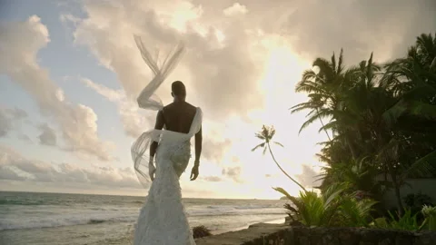 Non-binary black model in wedding dress poses on tropical beach near ocean at Stock Footage 251671042