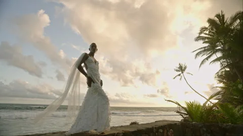 Non-binary black model in wedding dress poses on tropical beach near ocean at Stock Footage 252772553