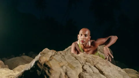 Non-binary black person crawls on all fours like wild cat on stone in water Stock Footage 241305147
