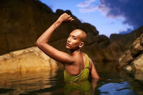 Non-binary black person stands chest deep in the middle of still water inside Stock Photos