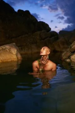 Non-binary black person stands chest deep in the middle of still water inside Stock Photos