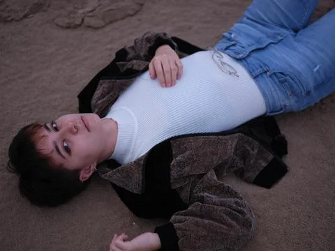 Non-binary girl posing lying on the sand on the beach and looking at the camera Stock-Fotos