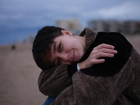 Non-binary girl sitting hugging her knees and looking sideways at the camera Stock Photos