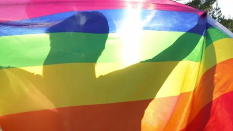 Non-binary guy waving rainbow flag with joy and spin backlighted in full sun Stock Footage 250468511
