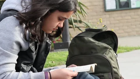Non binary kid reading book outside of a school Stock Footage 155387472