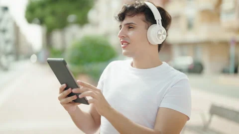 Non binary man smiling confident using touchpad and headphones at park Stock Footage 236761249