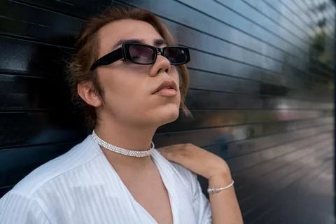 Non binary man with sunglasses leaning on black gate in the street remembering Stock Photos