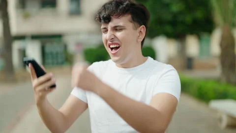 Non binary man talking on smartphone with winner expression at park Video stock 232876395