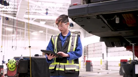 Non binary mechanic with digital tablet in bus maintenance facility Stock Footage 221036088