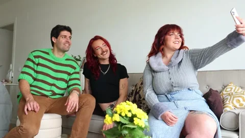 Non-binary person and plus-size friend taking selfies on sofa Stock Footage 309187523