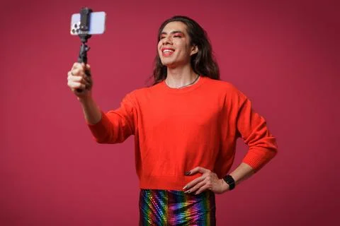 Non-binary person creating content with their cell phone on a red backgroun.. Stock Photos