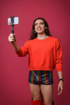 Non-binary person creating content with their cell phone on a red backgroun.. Stock Photos