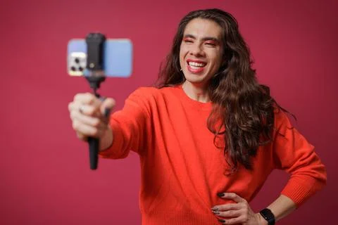 Non-binary person creating content with their cell phone on a red backgroun.. Stock Photos