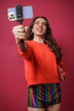 Non-binary person creating content with their cell phone on a red backgroun.. Stock Photos