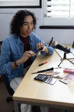 Non-binary person demonstrating makeup in denim shirt, holding palette, speaking 写真素材