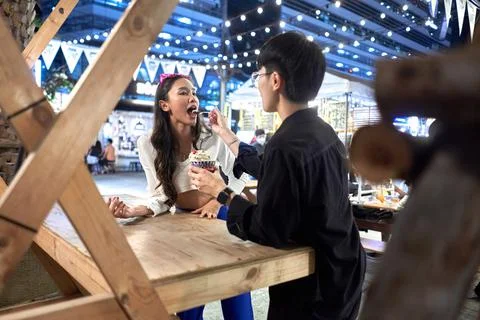 Non binary person feeding ice cream to her couple at urban night fair Stock Photos