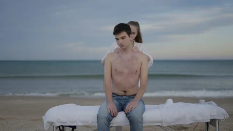 Non binary person gets back massage at the beach. Sits on massage table and Stock Footage 217411106