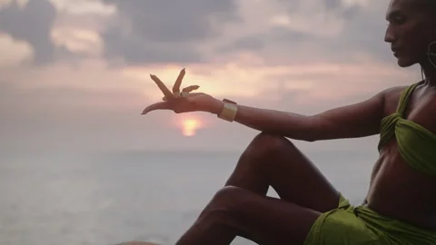 Non-binary person hand touches sun, poses gracefully sitting on top of rock in Stock Footage 276090286