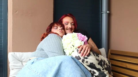 Non-binary person kissing chubby friend on a terrace Stock Footage 309130313