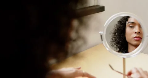 Non-binary person picking up spoolie and pencil at vanity mirror grooming brows Stock Footage 336609093