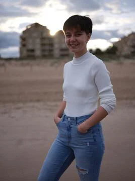 Non-binary person posing smiling on the beach with hands in pockets Stock-Fotos