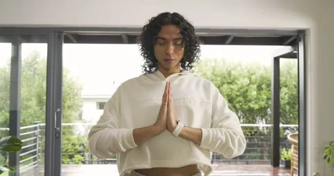 Non-binary person practicing meditation in prayer at sliding doors wearing Stock Footage 341240410