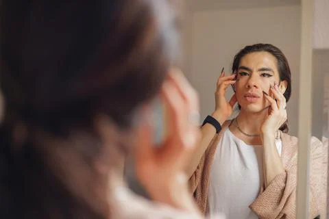 Non-binary person putting makeup on their face before going to work Stock Photos