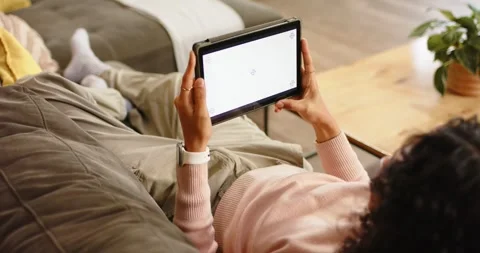 Non-binary person reclining on couch at home tapping blank tablet screen, Stock Footage 344534729