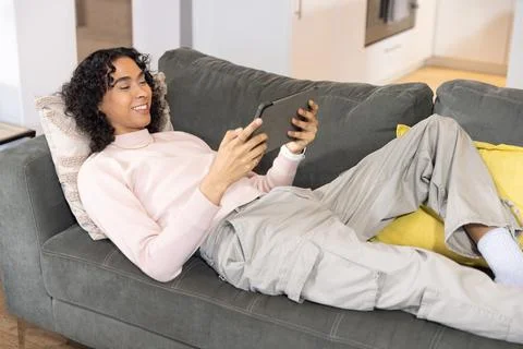 Non-binary person reclining on gray sofa at home in light-pink sweater and 写真素材