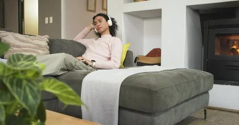 Non-binary person reclining on sectional couch in cozy living room wearing Stock Photos