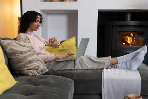 Non-binary person reclining on sofa at home wearing pink sweater, using laptop 写真素材