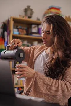 Non-binary person serving coffee at their desk to start the work day Stock Photos
