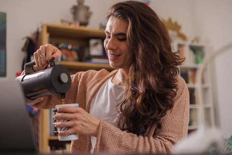 Non-binary person serving coffee at their desk to start the work day Stock Photos