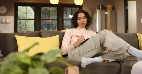 Non-binary person settling on sofa opening notebook, jotting pink pen notes and Stock Photos