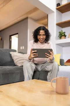 Non-binary person sitting and holding black tablet at home by coffee table 写真素材