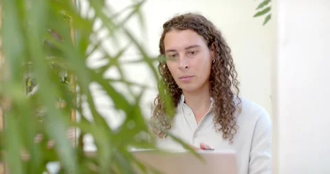 Non-binary person sitting at desk reading laptop, taking notes with pen for work Stock Footage 335748281