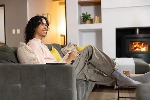 Non-binary person sitting on gray sofa in living room, wearing pink sweater, Stock Photos