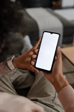 Non-binary person sitting on grey sofa at home holding smartphone wearing Stock Photos