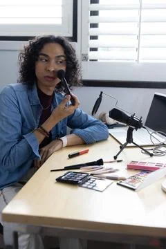 Non-binary person sitting at light wood desk applying makeup with brushes and 写真素材