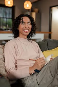 Non-binary person smiling and writing in notebook with pen on gray couch in Stock Photos