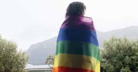 Non-binary person spotting mountain view adjusting rainbow flag, unfolding to Stock Footage 344946317
