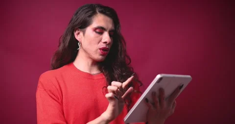 Non-binary person using a tablet on a red background and wearing pride clothing Stock Footage 309137665